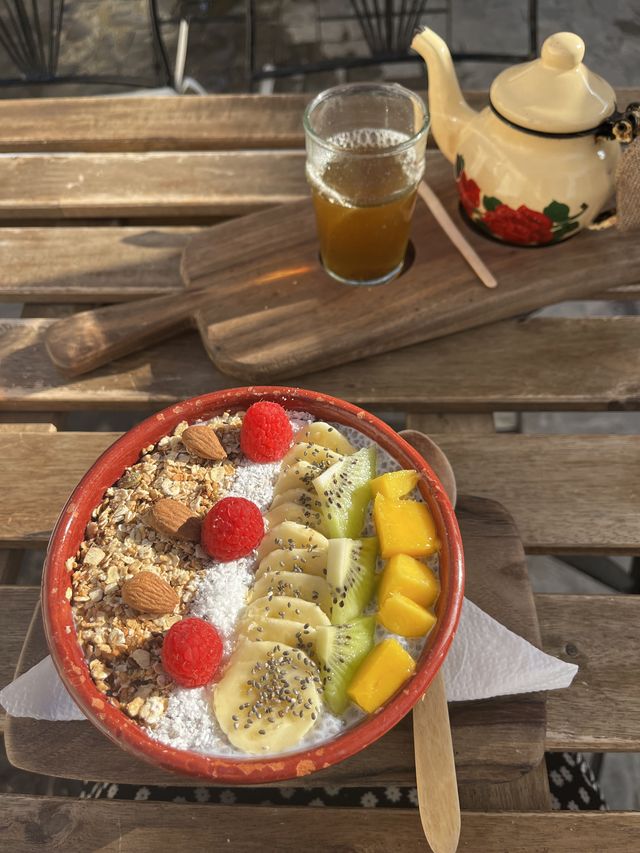 Bol de chia et granola garni de framboises, banane, kiwi, mangue et amandes, avec thé à la menthe