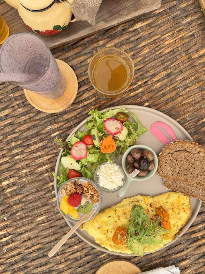Assiette petit-déjeuner : omelette à l'avocat, salade fraîche, fromage frais, olives, pain complet et bol de chia aux fruits