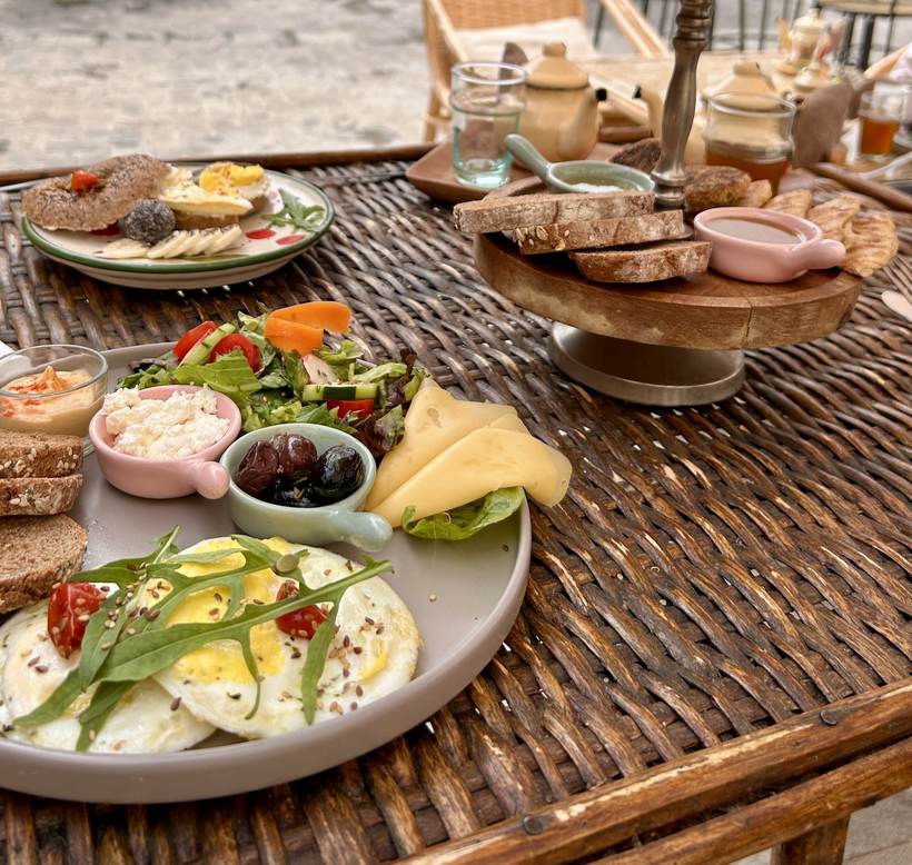 Planche brunch pour deux : œufs, avocat, salade, fromage frais, dattes, fruits et pain complet, sur table en rotin