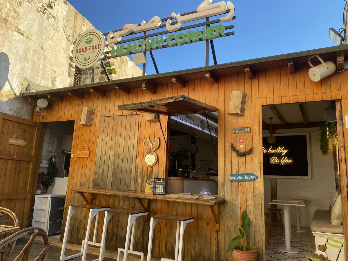 Le comptoir en bois de Good Food Healthy Corner sous son enseigne verte, avec tabourets et fenêtre de service sur la cuisine ouverte